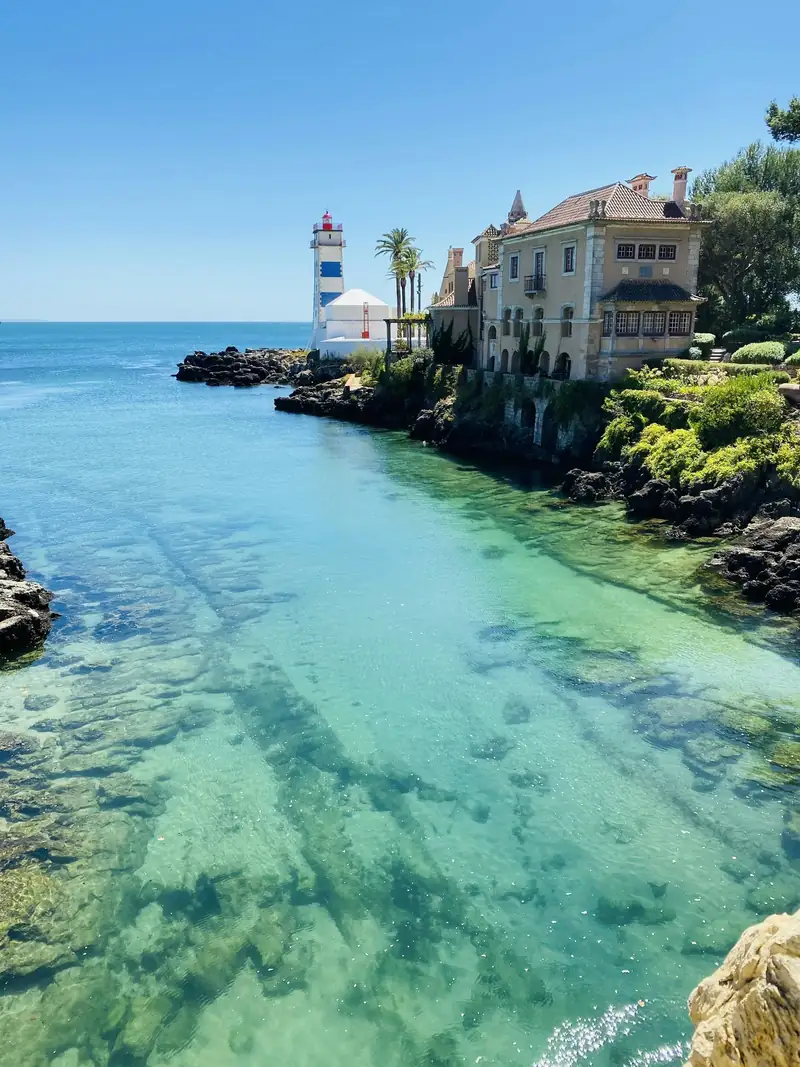 Farol de Santa Marta e casa senhorial junto a uma enseada de água transparente em Cascais
