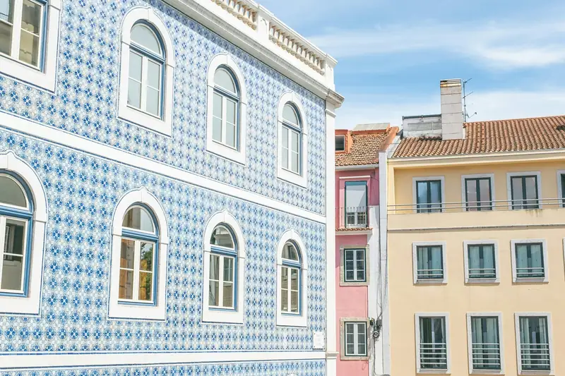 Fachada de azulejo azul e branco com janelas em arco, ao lado de prédios amarelos, na Estrela