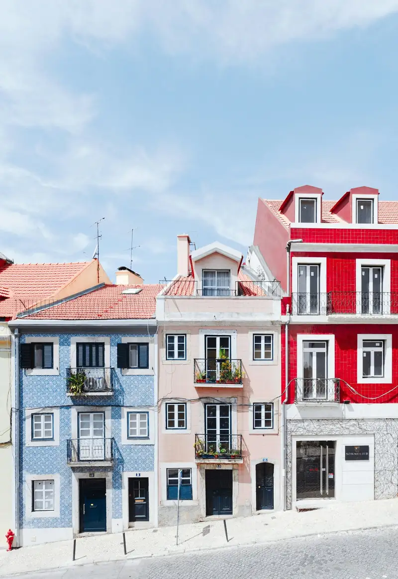Prédios estreitos de azulejo azul, rosa e vermelho lado a lado numa rua inclinada de Lisboa