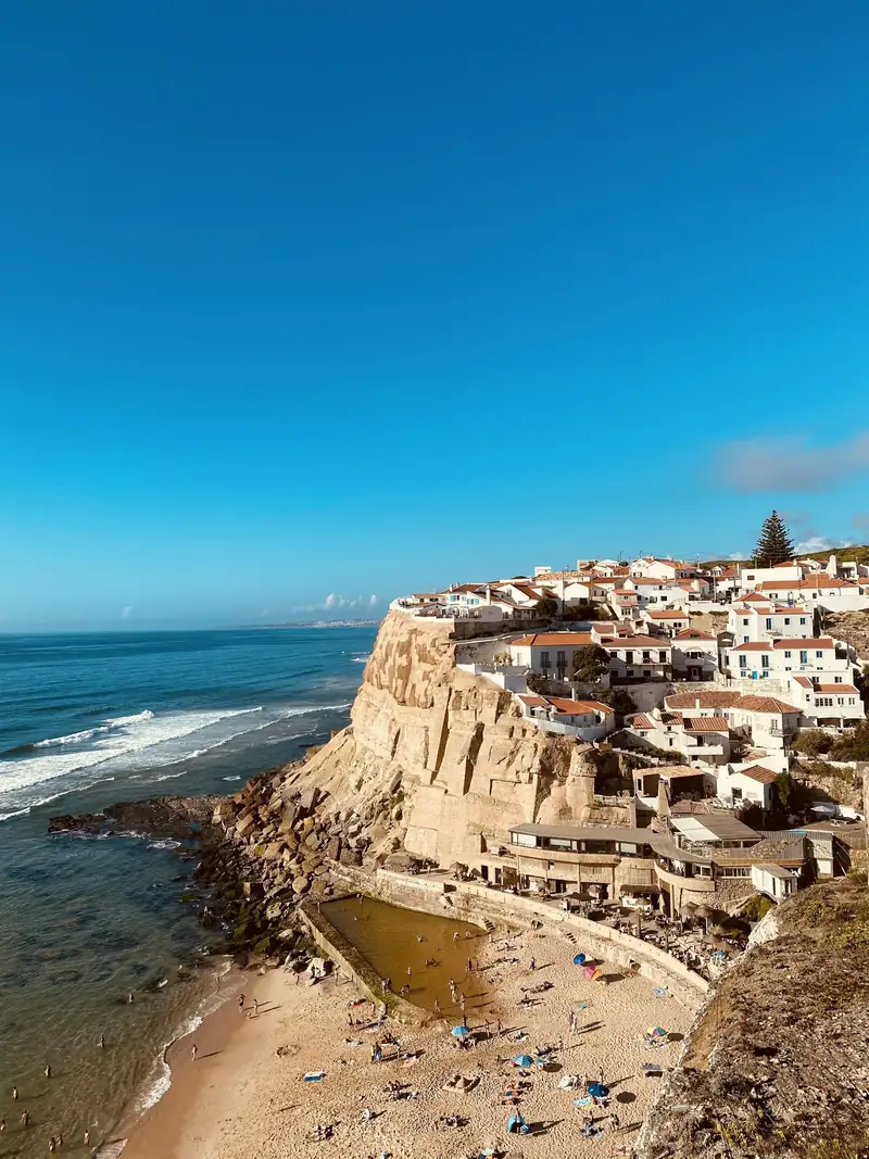 Casas brancas de Azenhas do Mar sobre a falésia, com a praia e a piscina natural em baixo